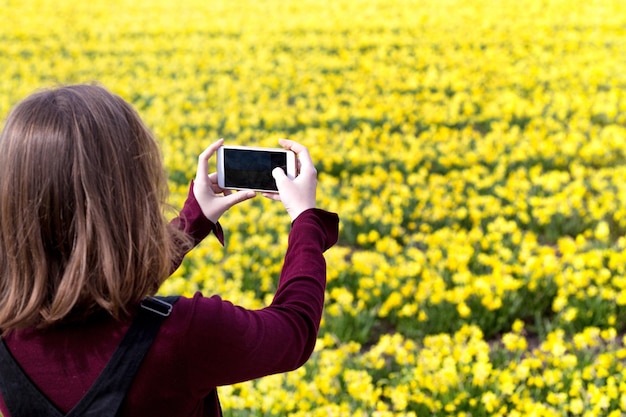 Chica toma fotos de narcisos amarillos en un teléfono inteligente