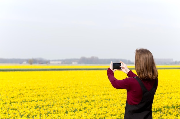 Chica toma fotos de narcisos amarillos en un teléfono inteligente