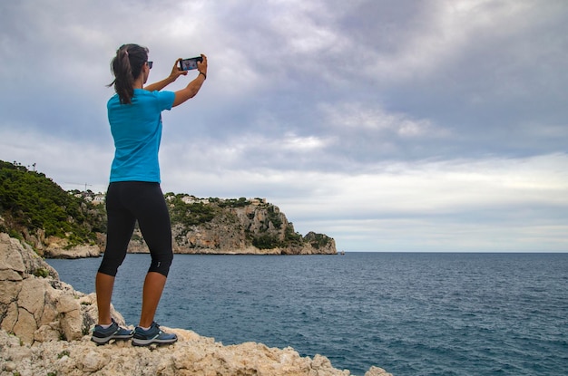 Chica tomando una foto de una costa rocosa con el teléfono inteligente