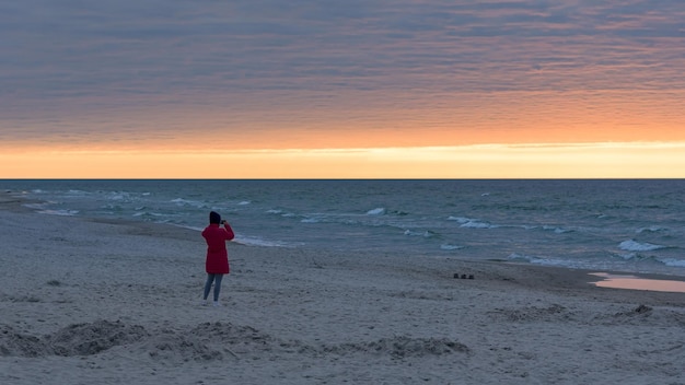 Chica tomando una foto de la puesta de sol en el mar