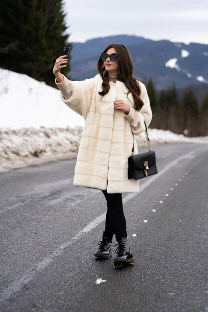 Chica tomando fotos de sí misma en el teléfono inteligente en las montañas de invierno