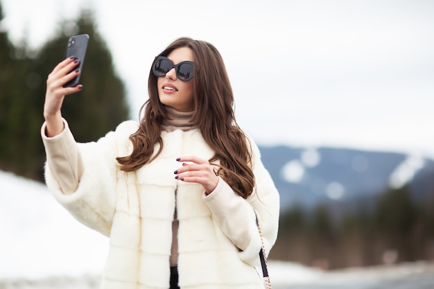 Chica tomando fotos de sí misma en el teléfono inteligente en las montañas de invierno