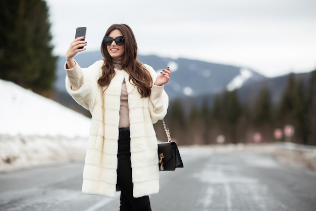 Chica tomando fotos de sí misma en el teléfono inteligente en las montañas de invierno