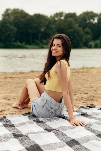 Una chica con un top amarillo se sienta en la playa y sonríe.