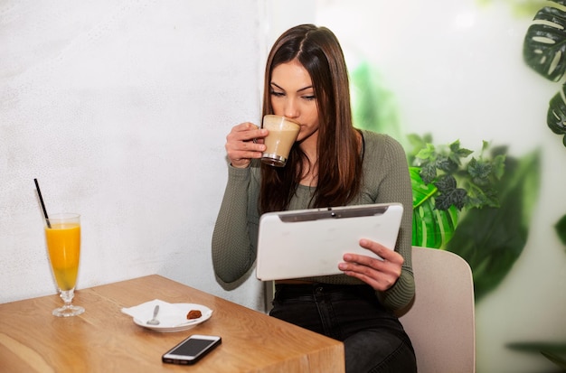 Chica trabaja desde la cafetería tomando café con tableta para trabajar