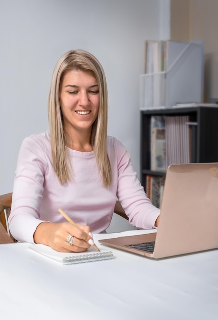 Chica trabaja en una computadora portátil y escribe en un cuaderno