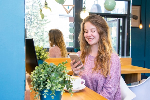 Chica trabaja en una computadora portátil para el trabajo remoto en un café