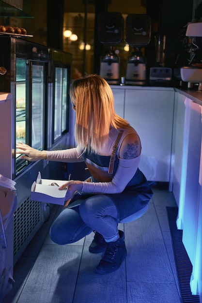 La chica trabajadora está quitando el pastel de una exhibición para un cliente en la panadería.