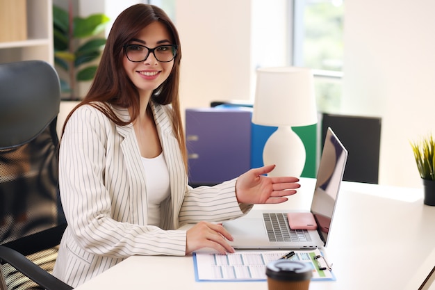 Chica trabajando en casa con portátil y sonriente, morena en chaqueta.