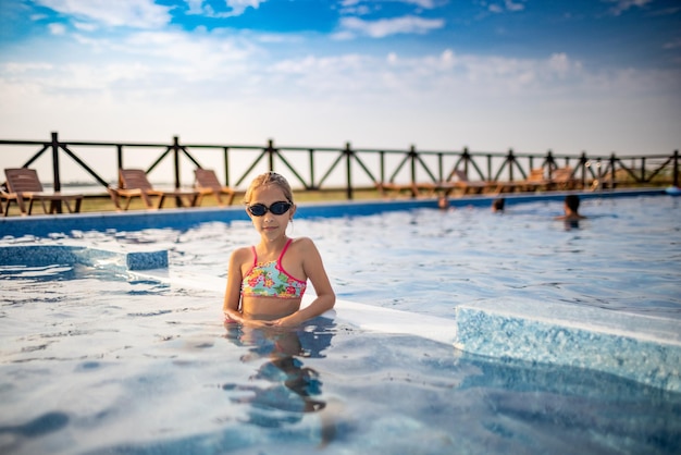 Una chica con un traje de baño brillante y gafas de natación posa cerca de la piscina tomando el sol bajo el sol de verano