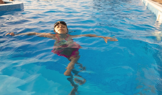 Una chica con un traje de baño brillante con gafas de natación se sumerge en una piscina con agua clara y transparente