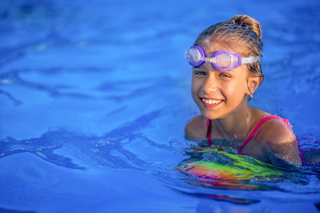 Una chica con un traje de baño brillante nada con una pelota inflable en una piscina con agua clara en una noche de verano