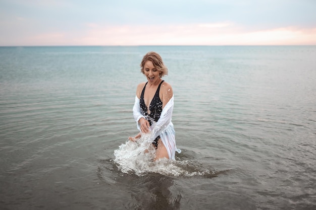 una chica con traje de baño negro y una camisa blanca está parada en el mar