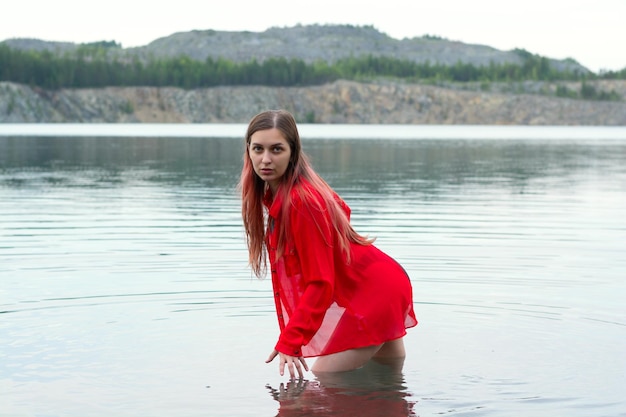 Una chica con traje de baño negro y camisa roja en el lago.