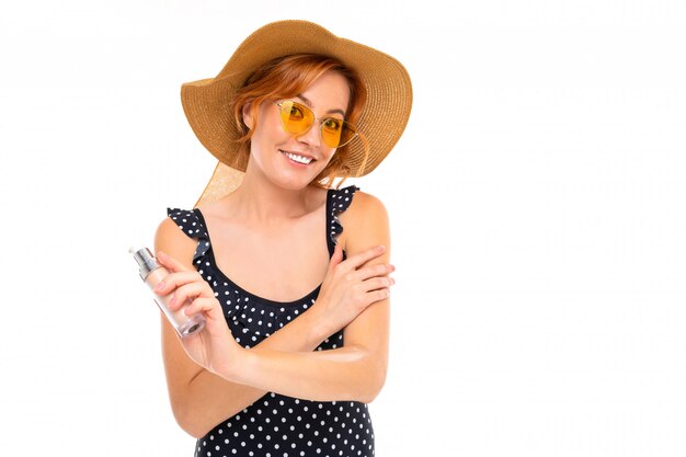 Chica en traje de baño retro y gafas de sol aplica bloqueador solar en una pared blanca