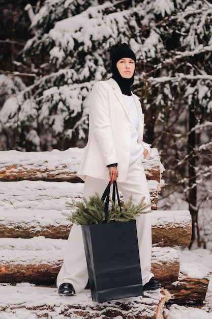 Una chica con traje blanco y pasamontañas con un paquete de árboles de Navidad en el bosque de invierno en la víspera de Año Nuevo Concepto de Año Nuevo