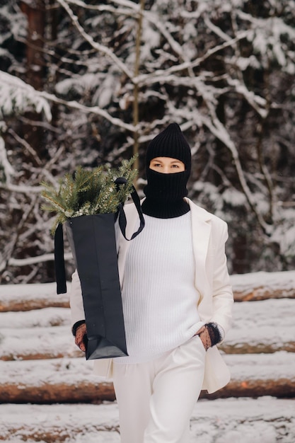 Una chica con traje blanco y pasamontañas con un paquete de árboles de Navidad en el bosque de invierno en la víspera de Año Nuevo Concepto de Año Nuevo