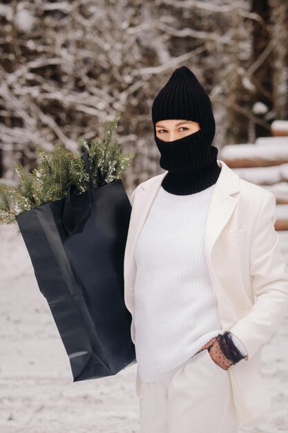 Una chica con traje blanco y pasamontañas con un paquete de árboles de Navidad en el bosque de invierno en la víspera de Año Nuevo Concepto de Año Nuevo