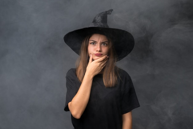 Chica con traje de bruja para fiestas de halloween sobre pared oscura aislada pensando en una idea