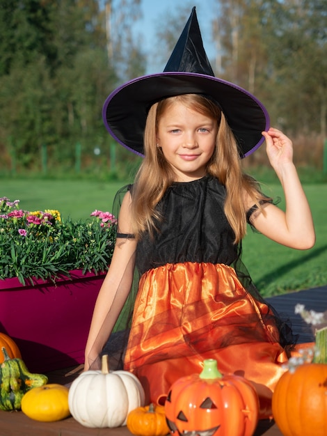 Chica en traje de bruja sentada con calabazas en la terraza de madera