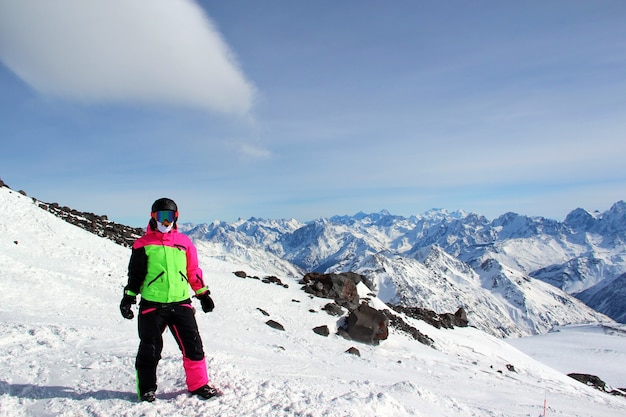 Chica con un traje colorido se encuentra en la cima de una montaña nevada