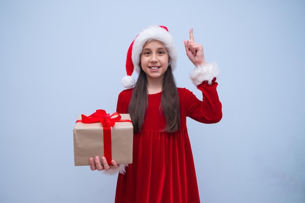 Chica en traje de santa tiene regalo para navidad apuntando con su dedo hacia arriba tiene un lugar ideal para publicidad