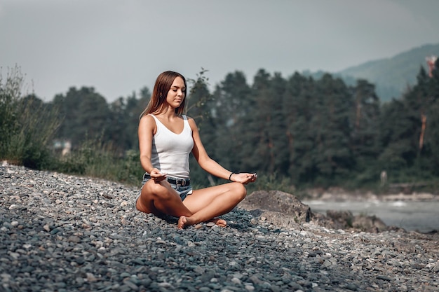 Chica tranquila y enfocada está meditando y preparándose junto al río en la naturaleza, retrato