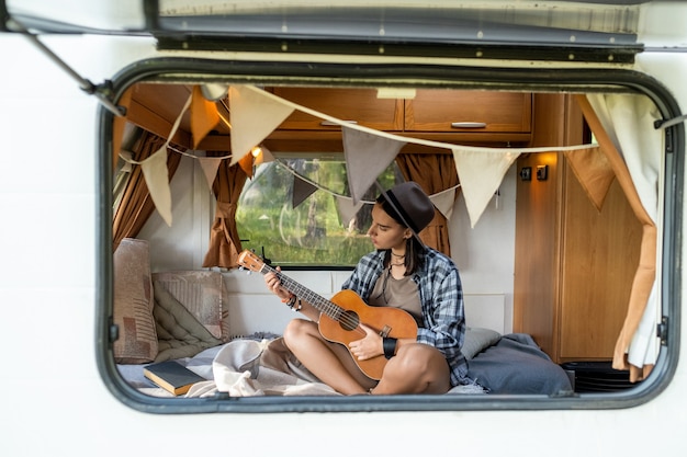 Chica tranquila en ropa casual tocando la guitarra dentro de casa sobre ruedas