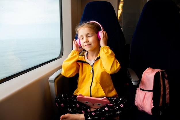 Una chica en un tren escucha música en auriculares con un aparato en sus manos Gadgets Vacaciones Verano