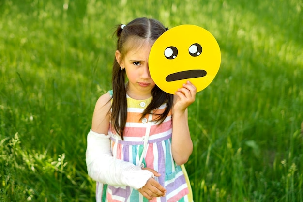 Foto una chica triste y frustrada con un yeso en el brazo roto sostiene un emoji lloroso