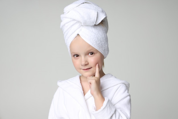 Chica con una túnica blanca y una toalla en la cabeza después de una ducha y lavarse el cabello. Cosmética infantil y cuidado de la piel, tratamientos de spa. Cabello limpio y hermoso.