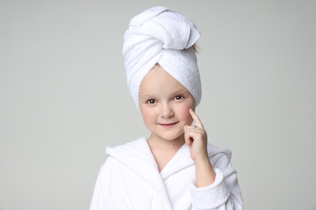 Chica con una túnica blanca y una toalla en la cabeza después de una ducha y lavarse el cabello