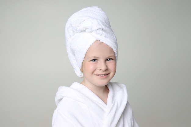 Chica con una túnica blanca y una toalla en la cabeza después de una ducha y lavarse el cabello.