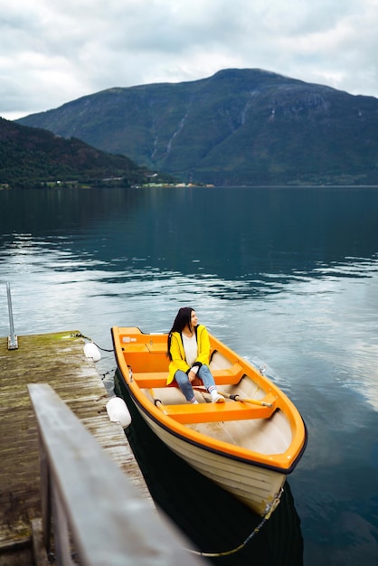 Chica turista con chaqueta amarilla está sentada posando en un bote en Noruega Aventura de estilo de vida itinerante