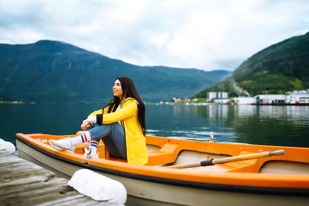 Chica turista con chaqueta amarilla está sentada posando en un bote en Noruega Aventura de estilo de vida itinerante