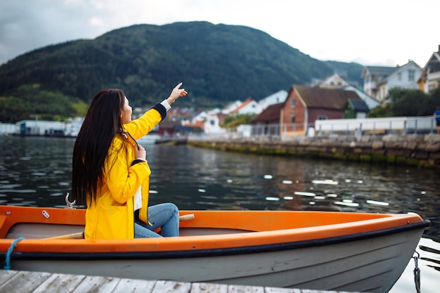 Chica turista con chaqueta amarilla está sentada y posando en un bote con el telón de fondo de las montañas