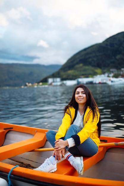 Chica turista con chaqueta amarilla está sentada y posando en un bote con el telón de fondo de las montañas