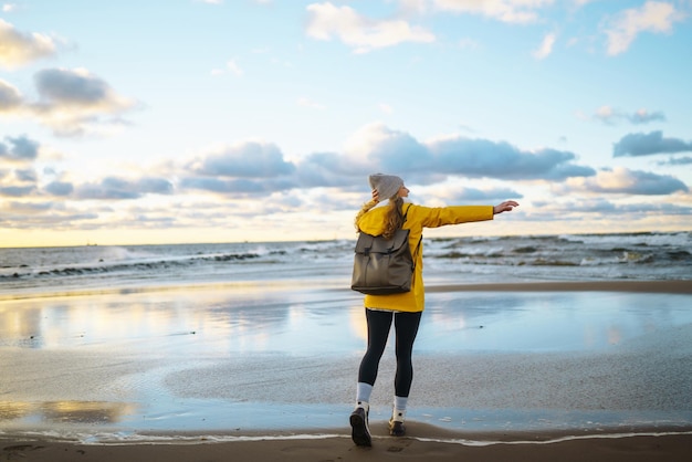 La chica turista con una chaqueta amarilla posando junto al mar Aventura de estilo de vida itinerante