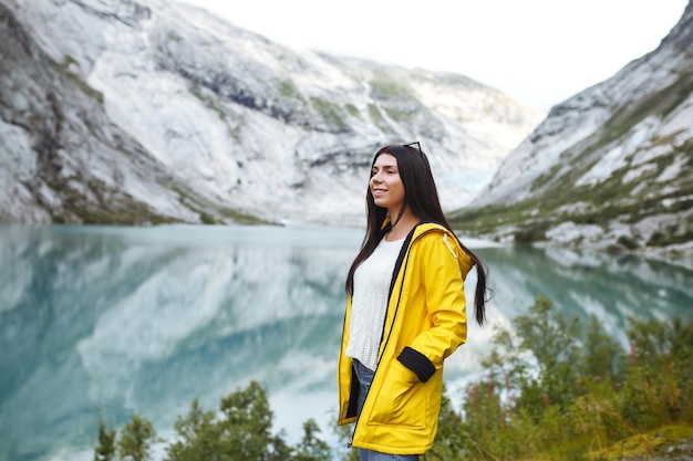 Chica turista en chaqueta amarilla posando en el lago en Noruega Mujer activa relajándose en Noruega