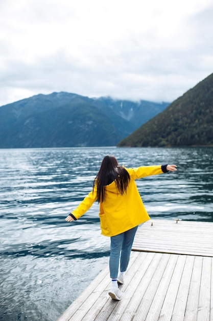 Chica turista en chaqueta amarilla posando en el lago en Noruega Mujer activa relajándose en Noruega