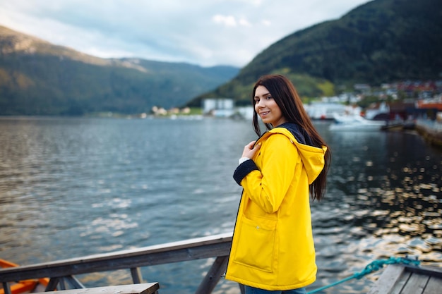 Chica turista en chaqueta amarilla posando en el lago en Noruega Mujer activa relajándose en Noruega