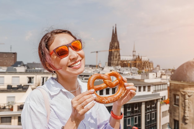 Chica turista feliz con un pretzel en el fondo de un edificio de la catedral de Colonia Viajes y turismo en Alemania y Renania