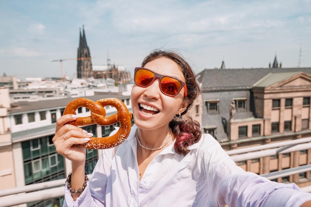 Chica turista feliz con un pretzel en el fondo de un edificio de la catedral de Colonia Viajes y turismo en Alemania y Renania