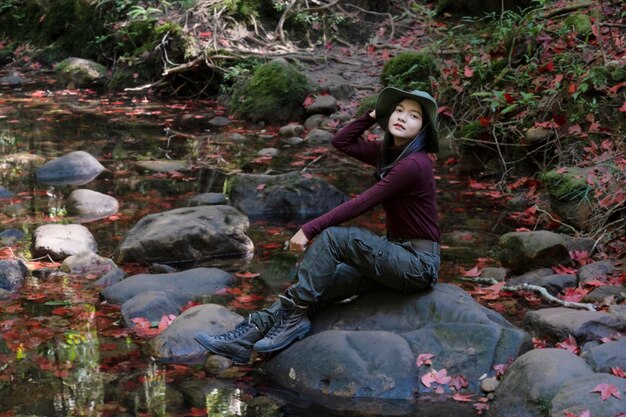 Chica turista feliz sentada en la piedra con una hermosa hoja de arce en la cascada Thamyai, Parque Nacional Phugradung Tailandia.