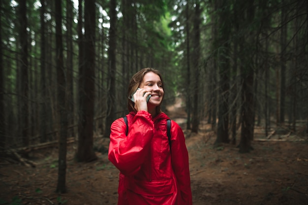 Chica turista hablando por teléfono en una caminata, de pie en el bosque