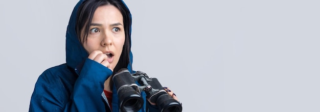 Una chica turista con un impermeable azul tiene binoculares en sus manos y mira a los espías a lo lejos