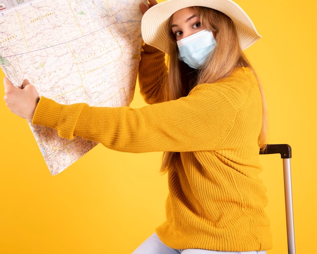 Foto una chica turista con una máscara médica, con una maleta, un sombrero que consulta un mapa, vuelos cancelados por covid-19