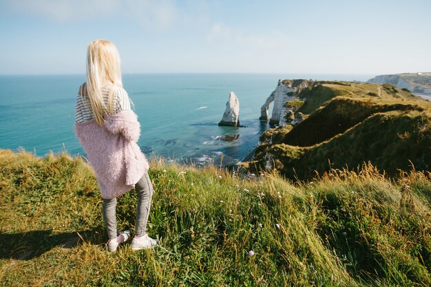 Chica turista mirando desde arriba a la bahía y el acantilado de alabastro bahía de Etretat, Francia