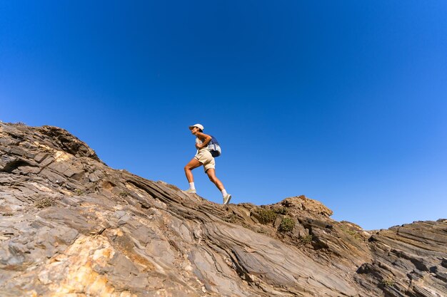 una chica turista con una mochila en la espalda sube la montaña en verano