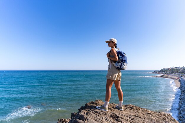 una chica turista con una mochila en la espalda en el verano se encuentra en la cima de una montaña